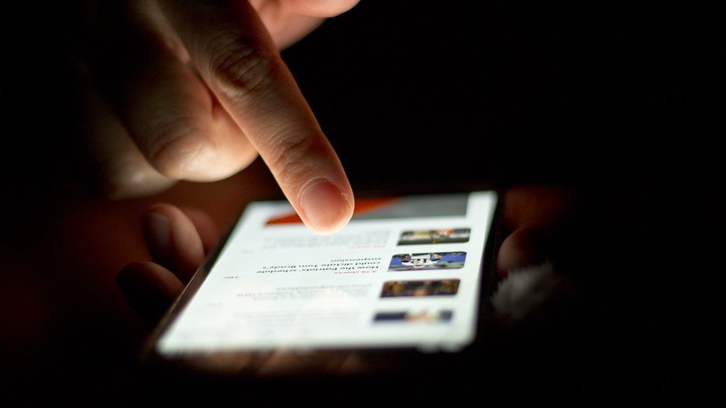 Persona che scorre un elenco di notizie su uno smartphone in una stanza poco illuminata
