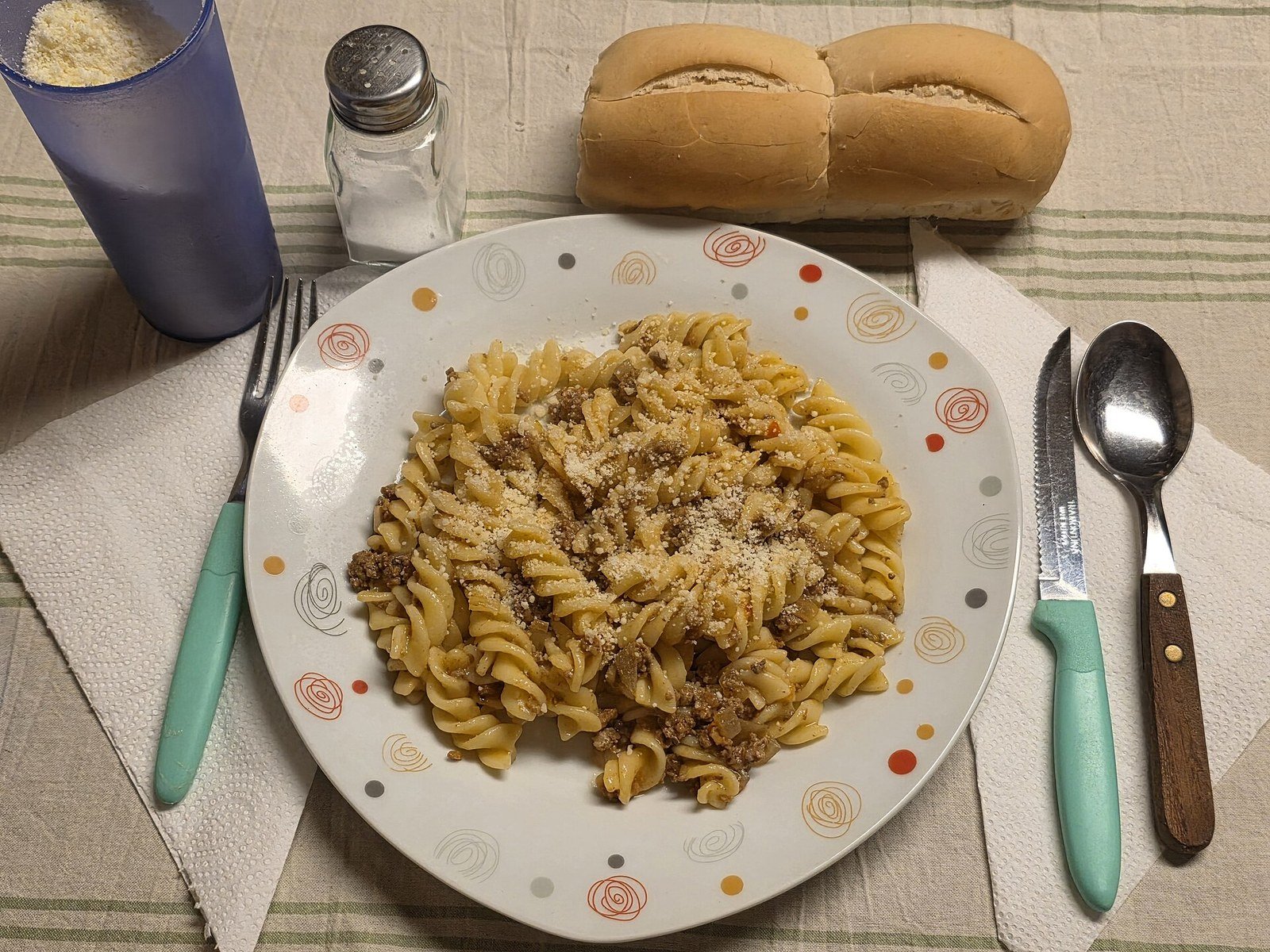 Piatto reale di pasta a spirale con condimento, pane e posate su una tavola